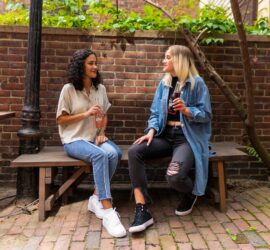 2 women sitting on brown wooden bench