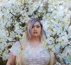 a woman with blue hair standing in front of a tree