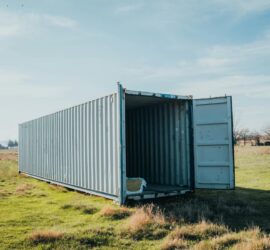 An open shipping container situated in a grassy field under a clear sky.