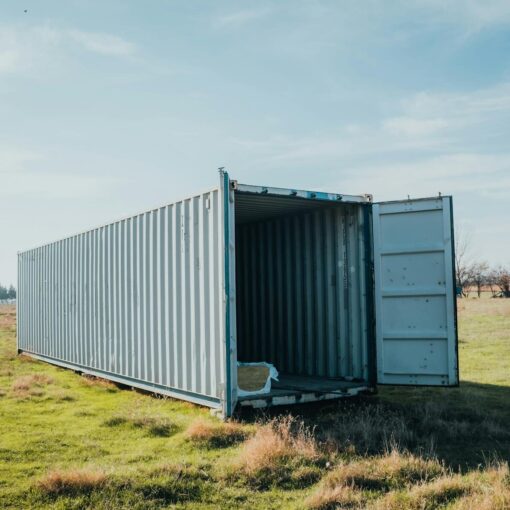 An open shipping container situated in a grassy field under a clear sky.